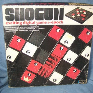 May include: A vintage "Shogun" board game box. The box is black with red and white game pieces. The game's title, "SHOGUN," is prominently displayed in large, bold letters. The box also includes the text "exciting digital game by epoch."