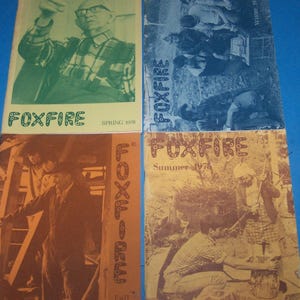 May include: Four vintage issues of the "Foxfire" magazine are displayed. The covers feature photographs and text, including the magazine's title and the season and year of publication. The color palette includes green, blue, orange, and brown.