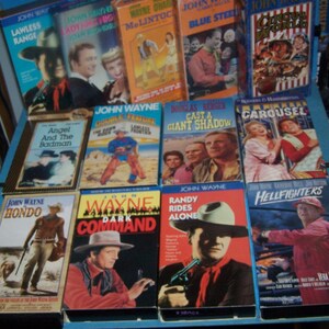 May include: A collection of VHS tapes featuring John Wayne in various Western films, including "Lawless Range", "Angel and the Badman", "Hondo", "The Dawn Rider", "Randy Rides Alone", "Hellfighters", "Cast a Giant Shadow", "Dark Command", "Circus World", "Blue Steel", "Lady for a Day", "McLintock", and "Carousel".