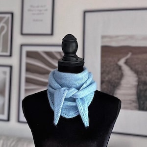 May include: A light blue knitted scarf with a delicate lace pattern, tied around a black mannequin's neck.