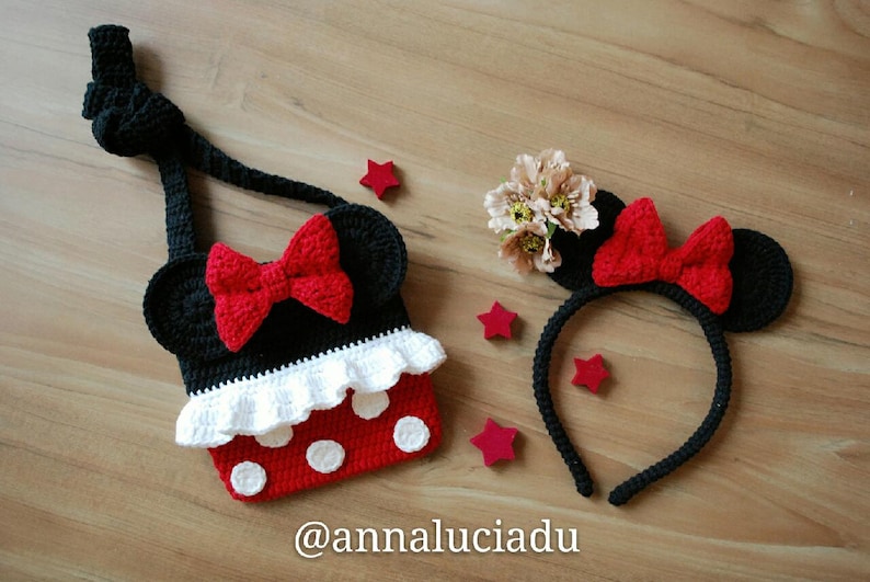 Pu&ograve; includere: Un cerchietto Minnie Mouse in crochet nero e rosso e una borsa abbinata con un volant bianco e pois rossi. Il testo "@annaluciadu" &egrave; sulla superficie in legno.