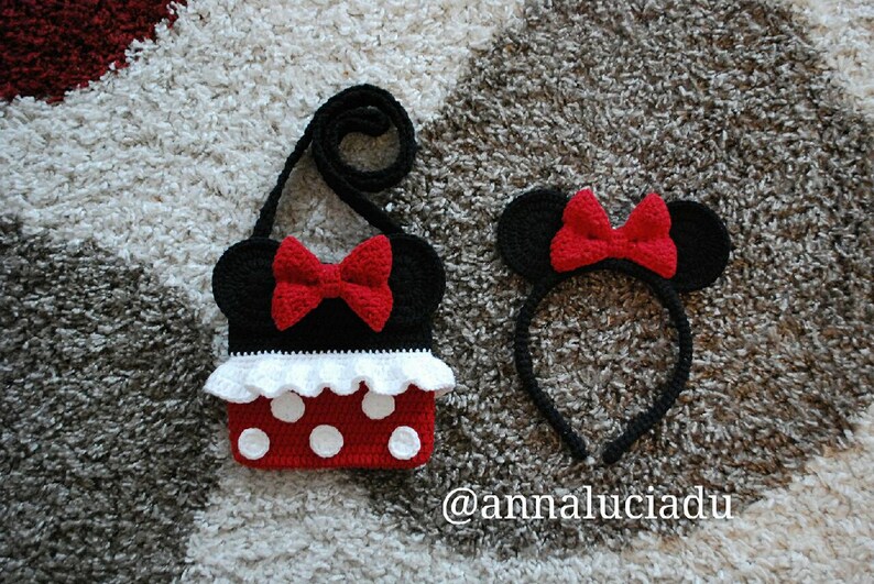 Pu&ograve; includere: Una borsa Minnie Mouse in crochet nero e rosso con un volant bianco e pois rossi. &Egrave; incluso anche un cerchietto abbinato in crochet nero e rosso con orecchie di Minnie Mouse. Il testo '@annaluciadu' &egrave; visibile nell'immagine.