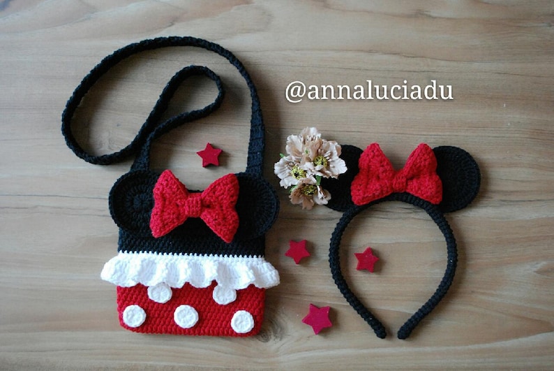 Pu&ograve; includere: Una borsa a tracolla in crochet nero a tema Minnie Mouse con un fiocco rosso e pois bianchi. La borsa ha una tracolla nera ed &egrave; abbinata a una fascia per capelli in crochet nero con fiocco rosso e orecchie nere.