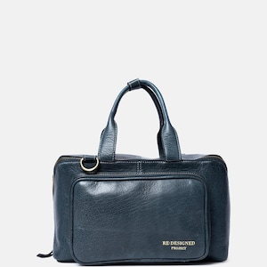 May include: A dark blue leather handbag with two top handles, a zippered main compartment, and a front pocket featuring a gold-toned metal D-ring. The front pocket displays the gold embossed text RE:DESIGNED PROJECT on the bottom right corner.