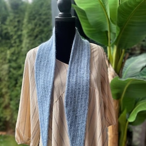 May include: A light blue knitted scarf with a pointed end, draped over a dress form with a beige and white striped dress.