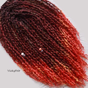 May include: Red, orange, and brown wool dreadlocks with beads. The dreadlocks are ombre, transitioning from dark brown to red and orange.