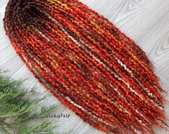 May include: A long strand of wool dreadlocks in shades of red, orange, brown, and white. The dreadlocks are twisted and textured, creating a unique and bohemian look.