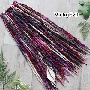 May include: A collection of handmade dreadlocks in various shades of purple, pink, gray, and brown. The dreads are arranged on a light wood surface. The text "VickyFelt" is visible in the upper right corner.