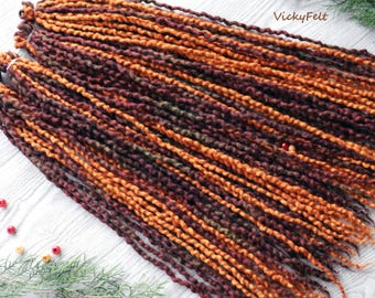 May include: A set of brown, orange, and green wool dreadlocks. The dreadlocks are made of yarn and are approximately 24 inches long. The dreadlocks are arranged in a fan shape on a white wooden surface.