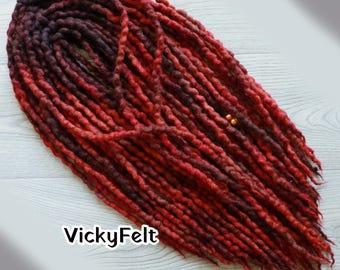 May include: A set of synthetic dreadlocks featuring a gradient color transition from deep dark burgundy at the roots to a vibrant bright red at the tips. The textured strands are arranged in a bundle and include two small gold-toned beads. The text VickyFelt is visible in the lower left corner.