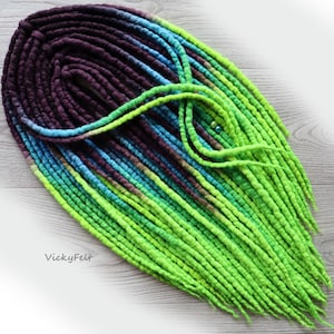 May include: A set of long, green, blue, and purple wool dreadlocks. The dreadlocks are arranged in a circle, with the ends of the dreadlocks hanging down.