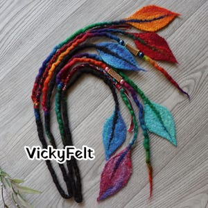 Peut inclure: Ensemble de dreadlocks faits à la main, colorés, avec des feuilles en feutre. Les dreadlocks sont un mélange de couleurs arc-en-ciel, et les feuilles sont dans des tons de bleu, rouge, orange et vert. Le texte "VickyFelt" est visible.