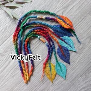 May include: Handmade rainbow dreadlock extensions with felted leaf accents. The dreadlocks are a vibrant mix of colours, transitioning from green to red and orange. The felt leaves are in shades of blue, orange, and yellow, with decorative beads. The text "VickyFelt" is visible.