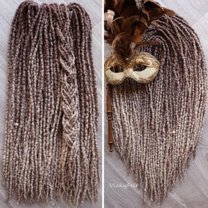 May include: Two sets of long, brown and beige wool dreadlocks, one set braided, with a gold and white masquerade mask in the background.