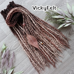 May include: Brown and beige dreadlocks with a decorative leaf and bead accent. The dreadlocks are arranged in a flowing pattern, with the text "VickyFelt" in the upper right corner. The dreadlocks are a mix of light and dark brown tones.