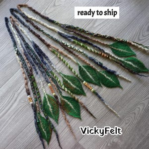 May include: A set of long, twisted felt hair extensions in shades of brown, cream, and dark blue, accented with green felt leaves and wooden beads. The image includes the text "ready to ship" and "VickyFelt" in white boxes.