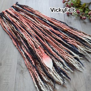 May include: A collection of handmade dreadlocks in various colors, including peach, navy, brown, and white. The dreadlocks are arranged on a wooden surface. The text "VickyFelt" is visible in the upper right corner.