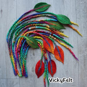 May include: A collection of colorful dreadlock extensions with felted leaf accents. The dreadlocks are a vibrant mix of rainbow hues, with green, red, and orange felt leaves. The image includes the text "VickyFelt".