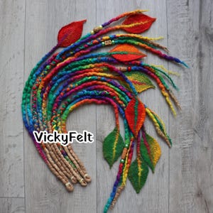 May include: Colorful dreadlock extensions with felted leaf accents. The dreads are a vibrant mix of rainbow colors, with brown tips. The leaves are red, orange, yellow, and green. The text "VickyFelt" is visible.