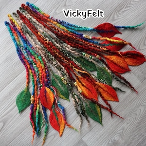 Op de afbeelding: Een verzameling kleurrijke, handgemaakte dreadlocks met vilten bladeren. De dreadlocks hebben een verscheidenheid aan kleuren, waaronder regenboog, rood, oranje en groen. De bladeren zijn in tinten groen, oranje en rood. De tekst "VickyFelt" is zichtbaar.
