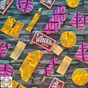 May include: A collection of Wonka Bar themed fabric scraps, including a Wonka Bar wrapper, a golden ticket, and a dummy clip. The fabric scraps are in various colours, including purple, pink, yellow, and gold. The fabric scraps are all decorated with the Wonka Bar logo and the words "Wonka's Golden Ticket".