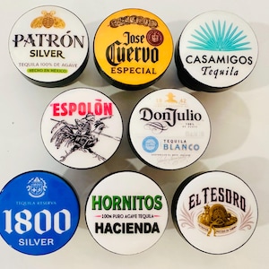 May include: A collection of eight round bottle stoppers featuring various tequila brand logos. Brands include Patrón Silver, Jose Cuervo Especial, Casamigos Tequila, Espolón, Don Julio Tequila Blanco, 1800 Silver, Hornitos Hacienda, and El Tesoro.