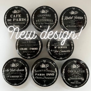 Puede incluir: Diez pomos redondos negros y blancos con varios nombres de tiendas parisinas y direcciones. Los pomos presentan un fondo negro con texto blanco y acentos florales decorativos.