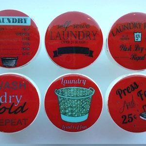 May include: Six red and white ceramic knobs with laundry-themed designs. The knobs feature text such as "Laundry", "Wash Dry Fold Repeat", "Press and Fold 25c", and "Laundry Loads of Fun".