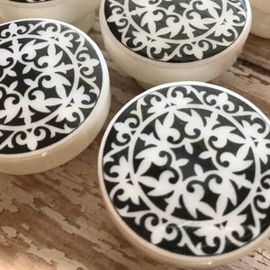 May include: Black and white ceramic knobs with a decorative floral pattern. The knobs are round and have a raised edge.