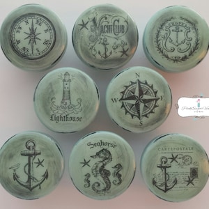 Könnte beinhalten: Neun runde, blaugrüne, hölzerne Knöpfe mit nautischen Motiven. Die Motive umfassen einen Kompass, einen Anker, einen Leuchtturm, ein Seepferdchen und ein Yachtclub-Logo.