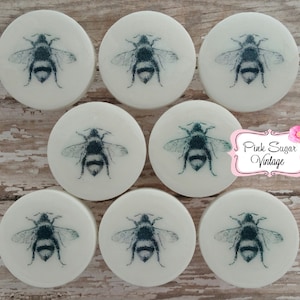 以下が含まれることがあります： 黒と白の蜂のイラストが描かれた白い丸い石鹸が8個。石鹸は2列4個ずつ並んでいます。背景には「Pink Sugar Vintage」の文字が見えます。