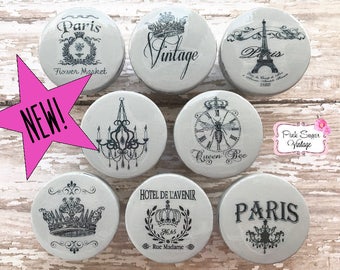 May include: Set of eight grey ceramic knobs with black and white vintage Parisian themed designs. The designs include a crown, a bee, a clock, a chandelier, the Eiffel Tower, and the words "Paris", "Vintage", and "Queen Bee".