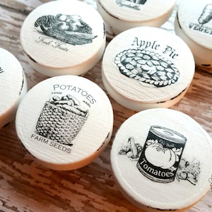 Peut inclure: Ensemble de 8 boutons ronds en c&eacute;ramique blanche avec des illustrations en noir et blanc de divers aliments. Les boutons portent les inscriptions "Rosemary", "Fresh Fruits", "Apple Pie", "Vegetables", "Potatoes", "Farm Seeds", et "Tomatoes".