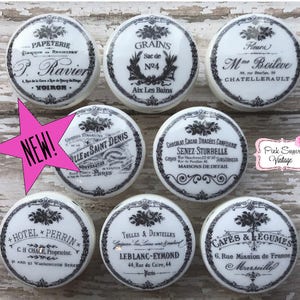 May include: Set of 8 vintage-style ceramic knobs with black and white designs. The knobs feature French text and images, including a hotel, grains, a shop, and a cafe.