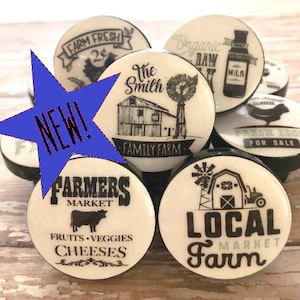 May include: Set of six white ceramic knobs with black lettering and images. The knobs feature farm-themed designs, including a farmhouse, a windmill, a cow, and a chicken. The text on the knobs includes "The Smith Family Farm", "Farmers Market", "Fresh Eggs For Sale", "Local Farm", "Organic Raw Milk", and "Farm Fresh 2¢".