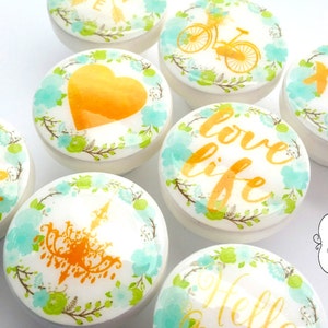 Puede incluir: Conjunto de ocho pomos de cerámica blanca con un diseño floral de acuarela turquesa y verde y letras doradas. Los pomos presentan las palabras "Love", "Love Life", "Hello", "XOXO", "Heart", "Bicycle", "Chandelier" y "Fleur de Lis".