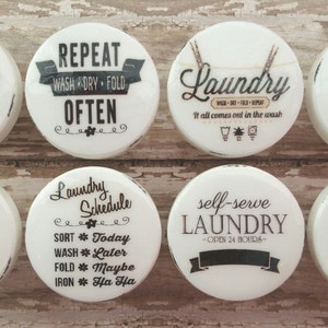 May include: Eight white round ceramic tiles with black lettering and designs. The tiles feature laundry room themed sayings such as "The Laundry Room", "Repeat Wash Dry Fold Often", "Laundry Schedule", "Self-Service Laundry Room", and "Laundry Room".