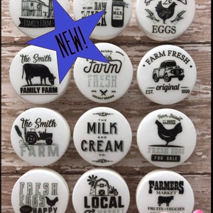 Puede incluir: Diez tapas redondas de cerámica blanca con diseños de temática agrícola en blanco y negro. Los diseños incluyen una granja, una vaca, un tractor, una gallina, una botella de leche, huevos y un camión. El texto en las tapas incluye "The Smith Family Farm", "Farm Fresh", "Organic Raw Milk", "The Milk and Cream Co.", "Farm Raised Fresh Eggs for Sale", "Local Market Farm", y "Farmers Market Fruits & Veggies".