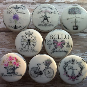May include: Set of 8 decorative round knobs with a distressed white finish. Each knob features a different Parisian-themed design, including a bee, a bicycle, a flower crown, and the Eiffel Tower. The knobs are perfect for adding a touch of French charm to any home.