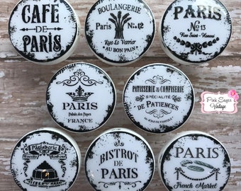 May include: Set of 8 black and white ceramic knobs with Parisian themed designs. The knobs feature text such as "Cafe de Paris", "Boulangerie", "Paris", "Pâtisserie & Confiserie", "Bistrot de Paris", and "French Market".