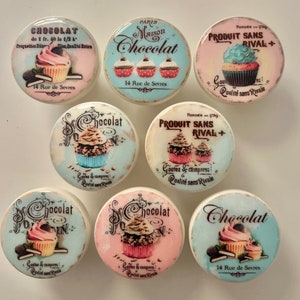 May include: Eight round ceramic tiles with a vintage design featuring cupcakes and the text "Chocolat". The tiles are decorated with pastel colours and have a distressed look. The text on the tiles includes "Maison Chocolat", "14 Rue de Sevres", "Fondee en 1739", "Produit Sans Rival", and "Goutez & Comparez! Qualite sans Rivale".