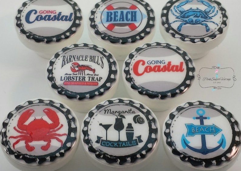 Peut inclure: Ensemble de boutons de placard en c&eacute;ramique blanche avec des motifs sur le th&egrave;me c&ocirc;tier. Les boutons pr&eacute;sentent des images de crabes, d'ancres, de cocktails et les phrases "Going Coastal" et "Beach". Chaque bouton a un design de bouchon de bouteille noir et blanc.