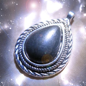 May include: A silver pendant with a dark gray teardrop-shaped stone set in a silver bezel. The pendant has a rope-like border and a silver loop for attaching a chain.