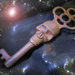 Może przedstawiać: Rustykalny metalowy klucz szkieletowy z ozdobną czaszką i dużym, ozdobnym otworem na klucz. Klucz leży na ciemnoniebieskim tle z tkaniny z białym, gwiaździstym wzorem.