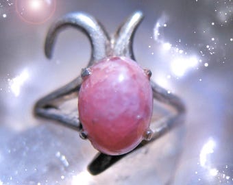 May include: A silver ring with a pink and white oval-shaped gemstone. The ring has a unique design with two curved prongs on either side of the stone.