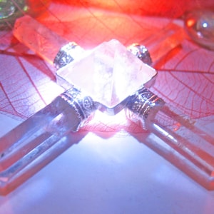 May include: A clear quartz crystal pyramid centerpiece featuring four radiating crystal points attached to a central square base with silver-toned metal caps. The structure is illuminated from beneath, casting a bright glow through the translucent stone points and the central pyramid structure.