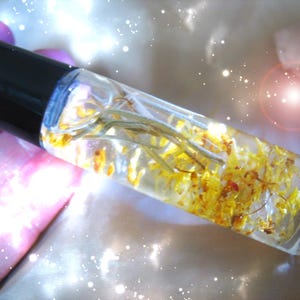 May include: A clear glass roller bottle filled with a yellow liquid and dried yellow flowers. The bottle has a black cap.