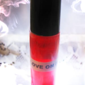 May include: A clear glass bottle with a black cap and a red liquid inside. The bottle has a white label with the text "LOVE ON" printed on it.