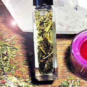 May include: A small glass bottle filled with a clear liquid and dried herbs. The bottle has a black cap and is sitting on a wooden surface.