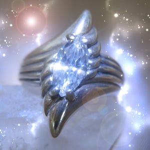 Könnte beinhalten: Ein silberner Ring mit einem großen, klaren, markisenförmigen Edelstein, der in einem einzigartigen, flügelartigen Design gefasst ist.